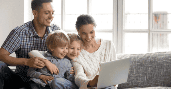 Family of four sitting on sofa smiling at the laptop