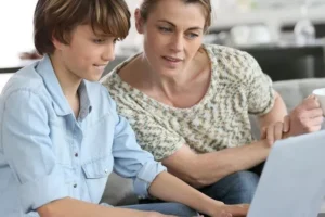 A mum and son look at a laptop together.